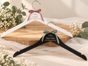 Percha blanca y percha negra personalizadas con nombres, fecha y lazos de tela.